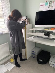 A lady wearing a grey dress is measuring an office desk using a tape measure. 